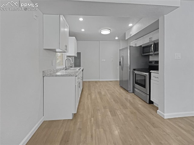 kitchen featuring appliances with stainless steel finishes, light stone countertops, sink, white cabinets, and light hardwood / wood-style flooring