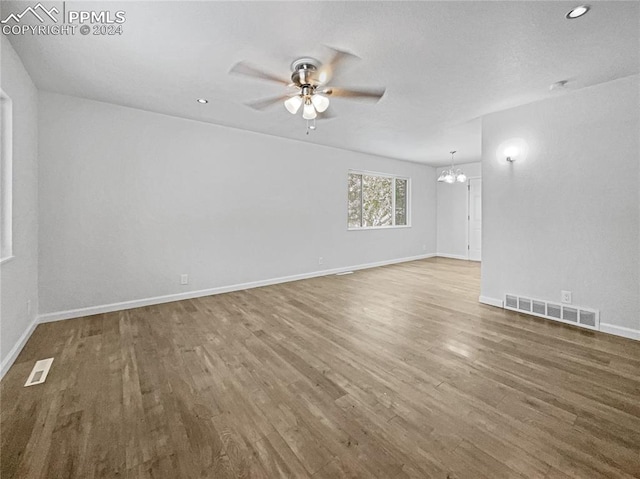 spare room featuring ceiling fan with notable chandelier and wood-type flooring