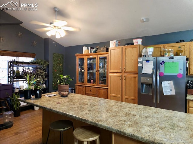 kitchen with light stone countertops, ceiling fan, a kitchen bar, stainless steel fridge with ice dispenser, and light wood-type flooring