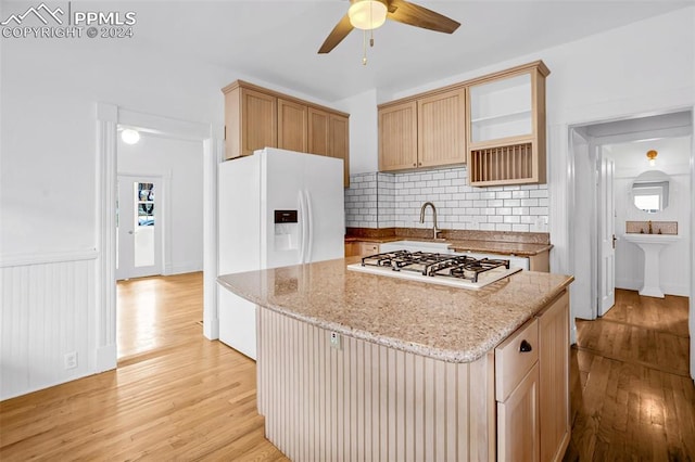 kitchen featuring decorative backsplash, a kitchen island, light stone countertops, light hardwood / wood-style flooring, and white appliances