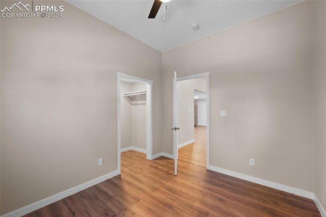 unfurnished bedroom featuring a spacious closet, ceiling fan, wood-type flooring, and a closet