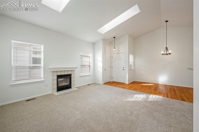 unfurnished living room with vaulted ceiling with skylight, a tile fireplace, and light hardwood / wood-style flooring