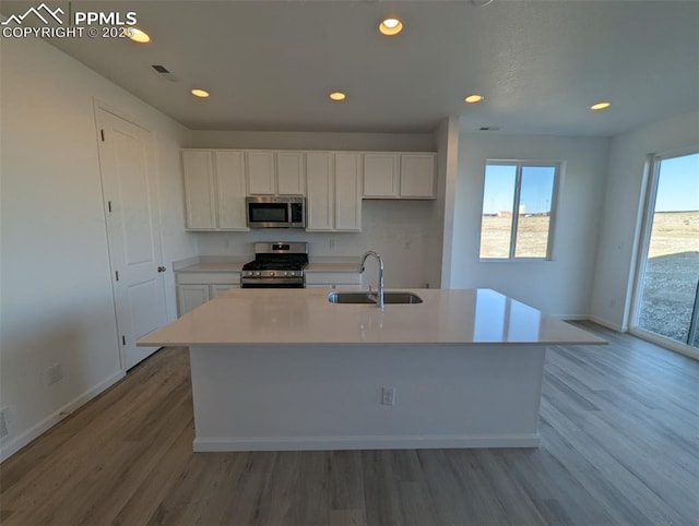 kitchen featuring sink, white cabinetry, light wood-type flooring, appliances with stainless steel finishes, and a kitchen island with sink