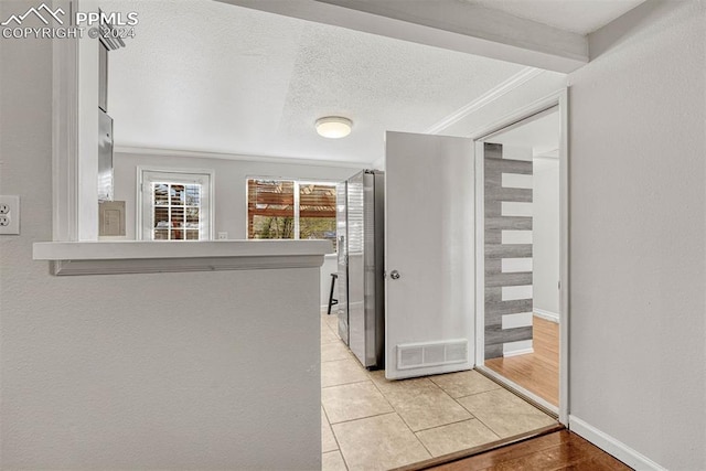 corridor with a textured ceiling, light wood-type flooring, and ornamental molding