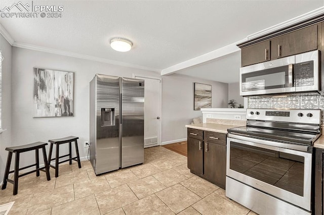 kitchen featuring dark brown cabinetry, stainless steel appliances, a textured ceiling, light tile patterned flooring, and ornamental molding