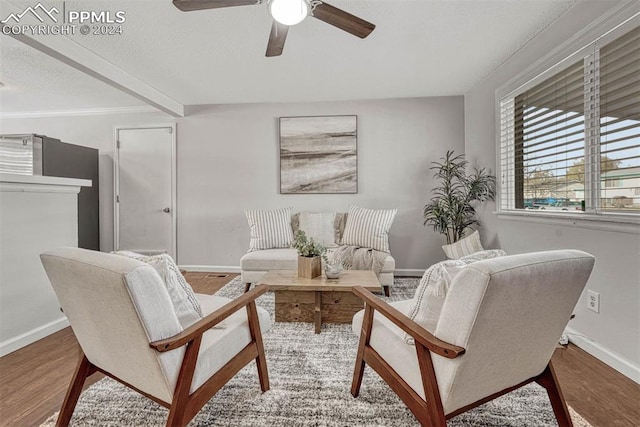 living area featuring beamed ceiling, wood-type flooring, and ceiling fan