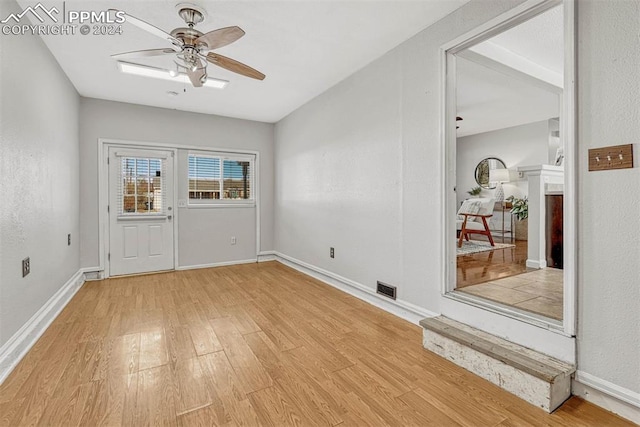 spare room with a stone fireplace, ceiling fan, and light hardwood / wood-style flooring