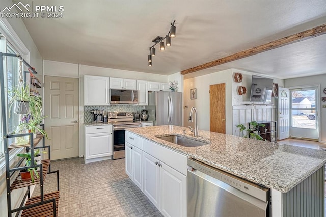 kitchen with stainless steel appliances, sink, light stone countertops, an island with sink, and white cabinets