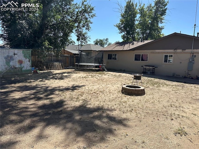 back of house featuring a trampoline and an outdoor fire pit