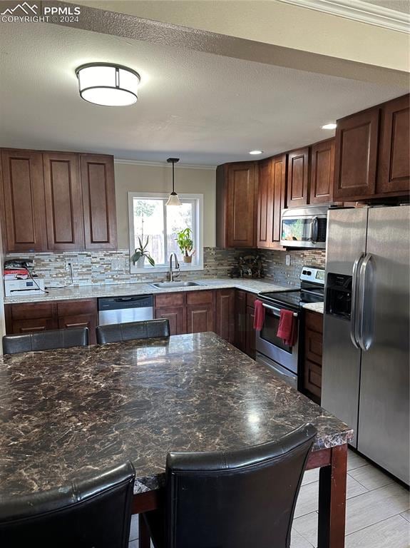 kitchen featuring sink, hanging light fixtures, stainless steel appliances, tasteful backsplash, and a kitchen bar