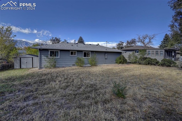 back of house featuring a mountain view, a storage unit, and a lawn