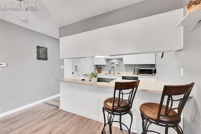 kitchen with white cabinets, light wood-type flooring, a textured ceiling, kitchen peninsula, and a breakfast bar area