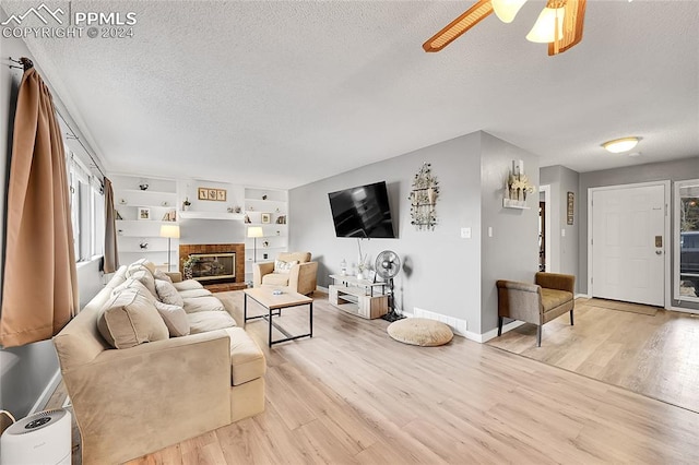 living room with ceiling fan, light wood-type flooring, and a textured ceiling