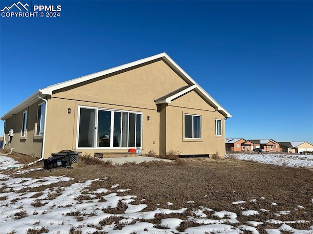 snow covered back of property with stucco siding