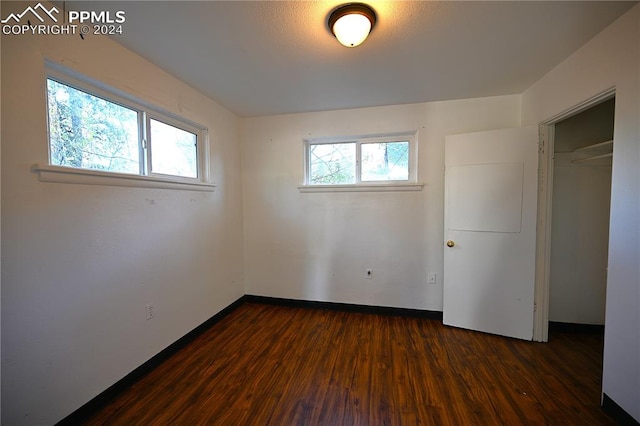 unfurnished bedroom with multiple windows, a closet, and dark hardwood / wood-style floors