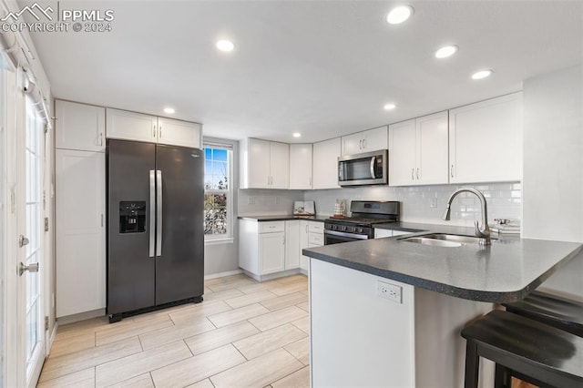 kitchen featuring sink, appliances with stainless steel finishes, white cabinetry, kitchen peninsula, and a breakfast bar area