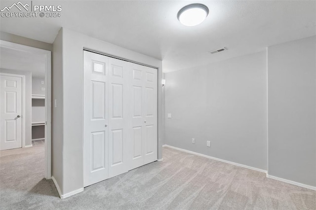 unfurnished bedroom with light colored carpet and a closet