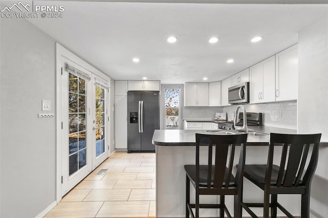 kitchen featuring kitchen peninsula, stainless steel appliances, sink, white cabinets, and a breakfast bar area