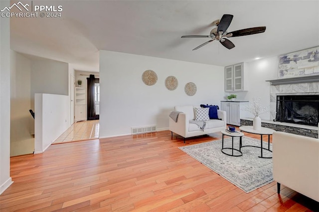 living room with a tiled fireplace, ceiling fan, and light wood-type flooring