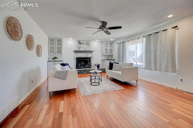 living room featuring light hardwood / wood-style flooring, ceiling fan, and a tiled fireplace