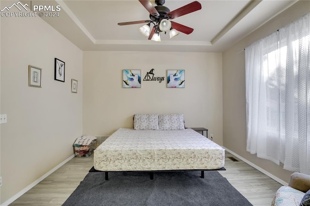 bedroom with a tray ceiling, ceiling fan, and light wood-type flooring