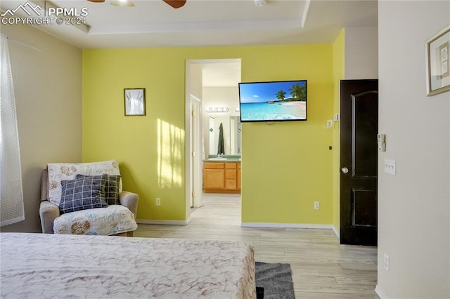 bedroom featuring a raised ceiling, ensuite bath, ceiling fan, and light hardwood / wood-style floors