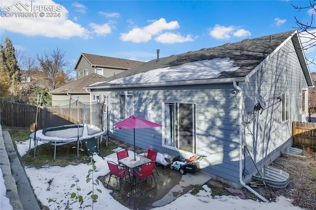 snow covered rear of property with a trampoline