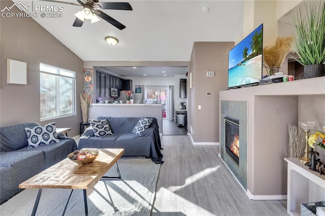 living room with a tile fireplace, ceiling fan, light hardwood / wood-style flooring, and vaulted ceiling