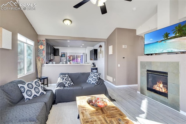 living room featuring ceiling fan, a fireplace, vaulted ceiling, and light wood-type flooring