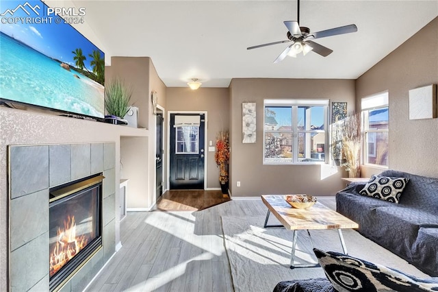 living room featuring a tiled fireplace, ceiling fan, lofted ceiling, and light wood-type flooring