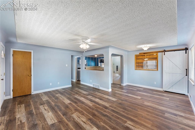 unfurnished living room featuring dark hardwood / wood-style floors, a barn door, a textured ceiling, and ceiling fan