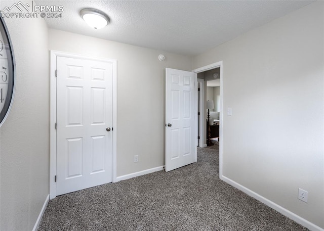 unfurnished bedroom with a textured ceiling and dark carpet