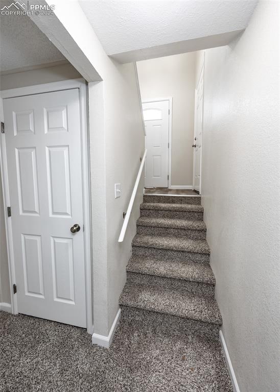 staircase with a textured ceiling and carpet flooring