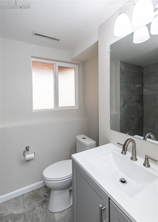 bathroom featuring a tile shower, vanity, a textured ceiling, and toilet