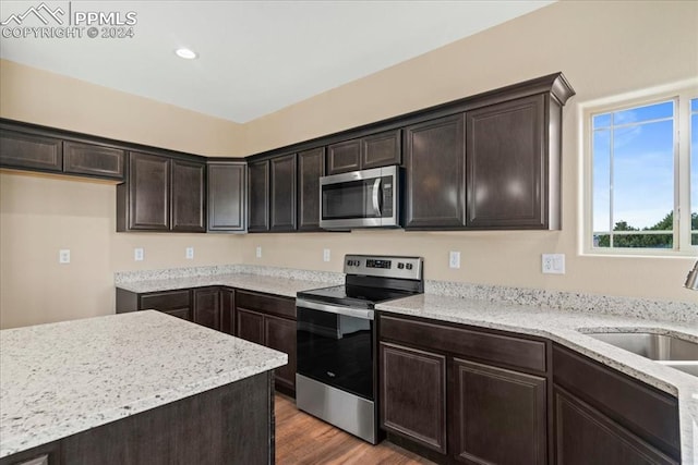 kitchen featuring dark brown cabinetry, sink, appliances with stainless steel finishes, light stone countertops, and wood-type flooring