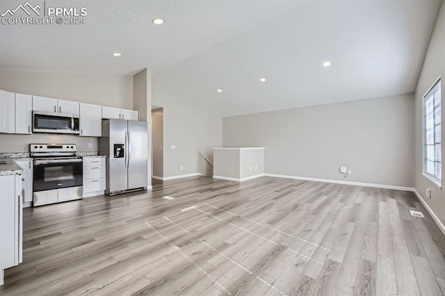 kitchen with white cabinets, vaulted ceiling, light hardwood / wood-style floors, and appliances with stainless steel finishes