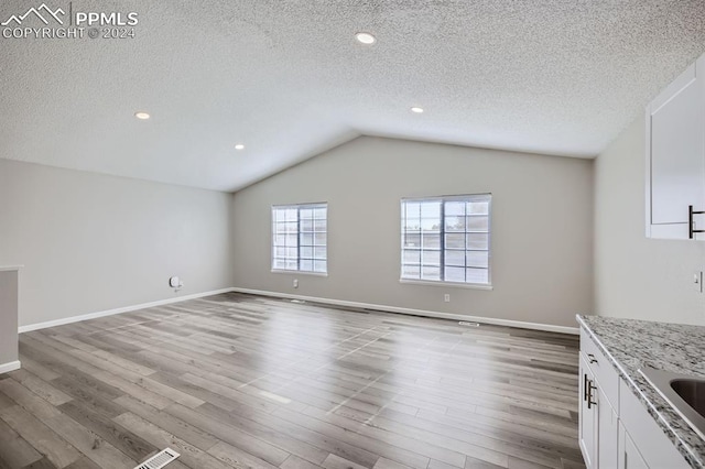 unfurnished living room featuring lofted ceiling, a textured ceiling, and light hardwood / wood-style flooring