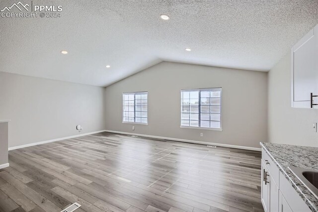 966 Daffodil St, Fountain, CO 80817 - unfurnished living room featuring wood finished floors, a textured ceiling, vaulted ceiling, baseboards, and recessed lighting