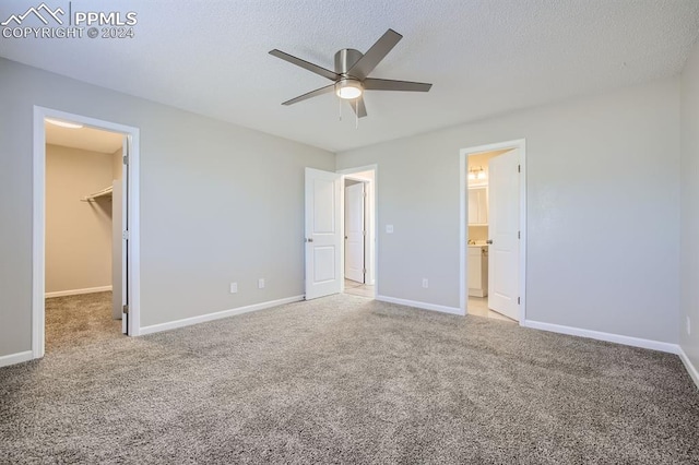 unfurnished bedroom featuring a closet, a spacious closet, carpet floors, a textured ceiling, and ceiling fan