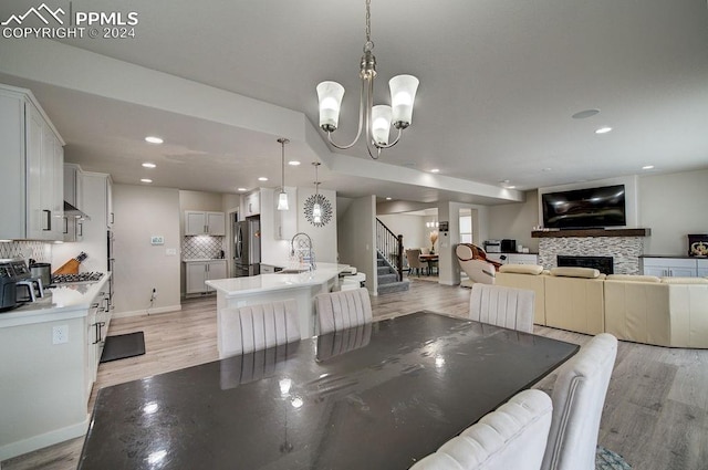 dining room featuring a stone fireplace, sink, light hardwood / wood-style floors, and a notable chandelier