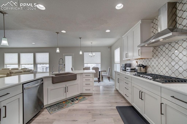 kitchen with sink, hanging light fixtures, wall chimney range hood, plenty of natural light, and appliances with stainless steel finishes