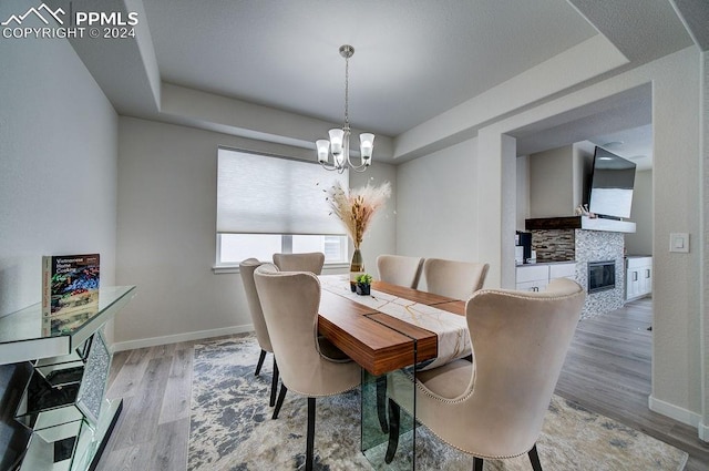 dining area with a tray ceiling, a stone fireplace, wood-type flooring, and an inviting chandelier