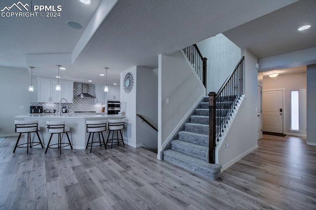 kitchen with pendant lighting, white cabinets, wall chimney exhaust hood, light hardwood / wood-style floors, and kitchen peninsula