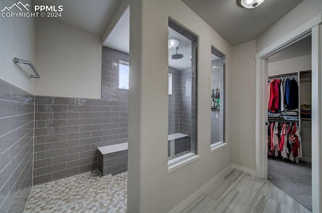 bathroom featuring a textured ceiling, tiled shower, and tile walls