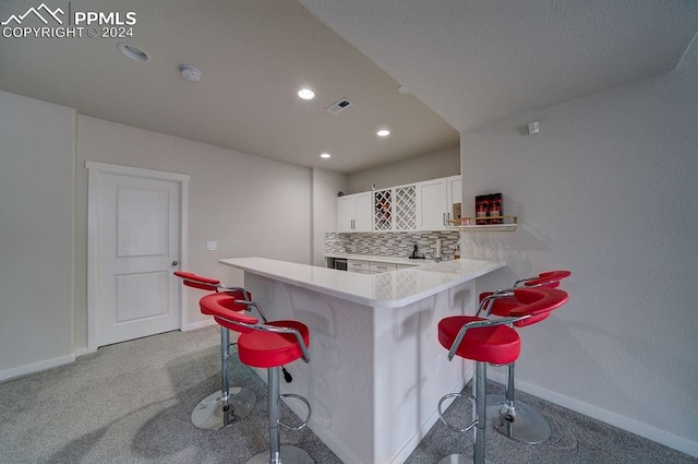 bar with white cabinets, decorative backsplash, and light colored carpet