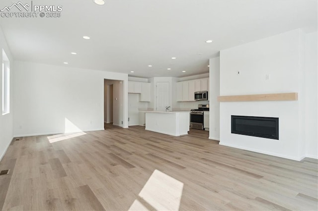 unfurnished living room featuring light wood finished floors, recessed lighting, visible vents, a glass covered fireplace, and baseboards