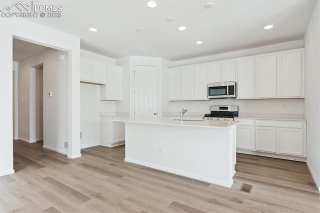 kitchen featuring appliances with stainless steel finishes, white cabinets, light countertops, and a center island with sink