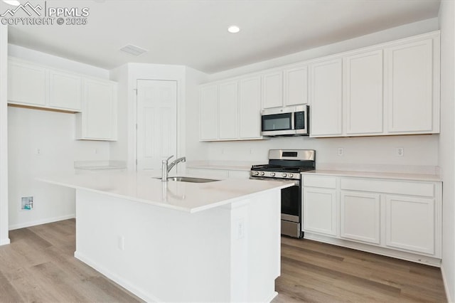 kitchen featuring white cabinets, an island with sink, stainless steel appliances, light countertops, and a sink