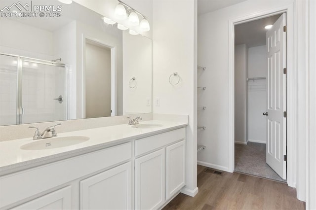 bathroom featuring double vanity, a sink, a shower stall, and wood finished floors