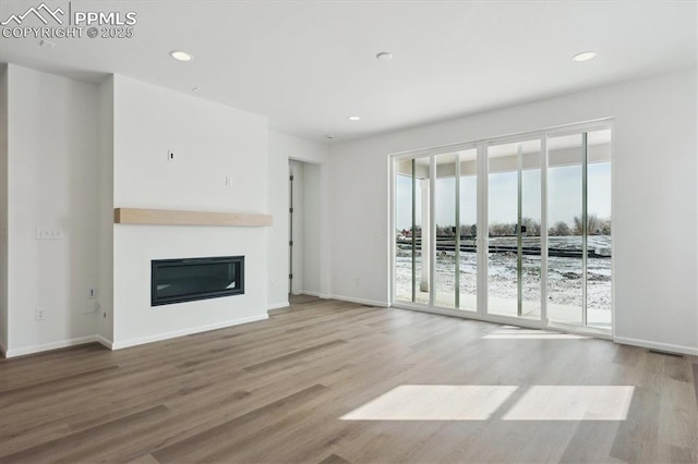 unfurnished living room with recessed lighting, light wood-style flooring, baseboards, and a glass covered fireplace